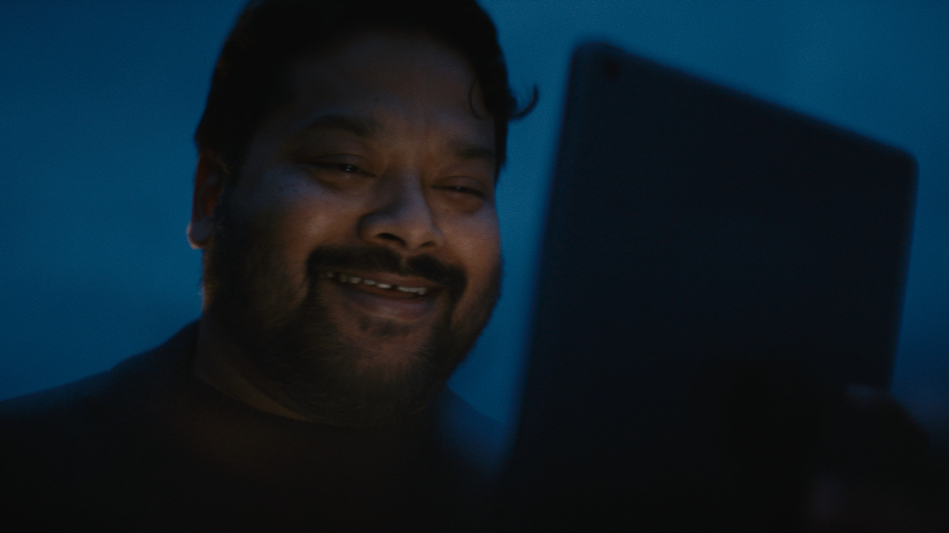 A man smiles as he looks at a tablet that lights up his face. A man smiles as he looks at a tablet that lights up his face.