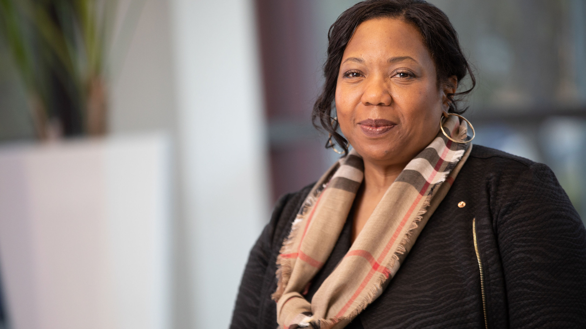 A woman in a black sweater and striped scarf smiles at the camera. A woman in a black sweater and striped scarf smiles at the camera.