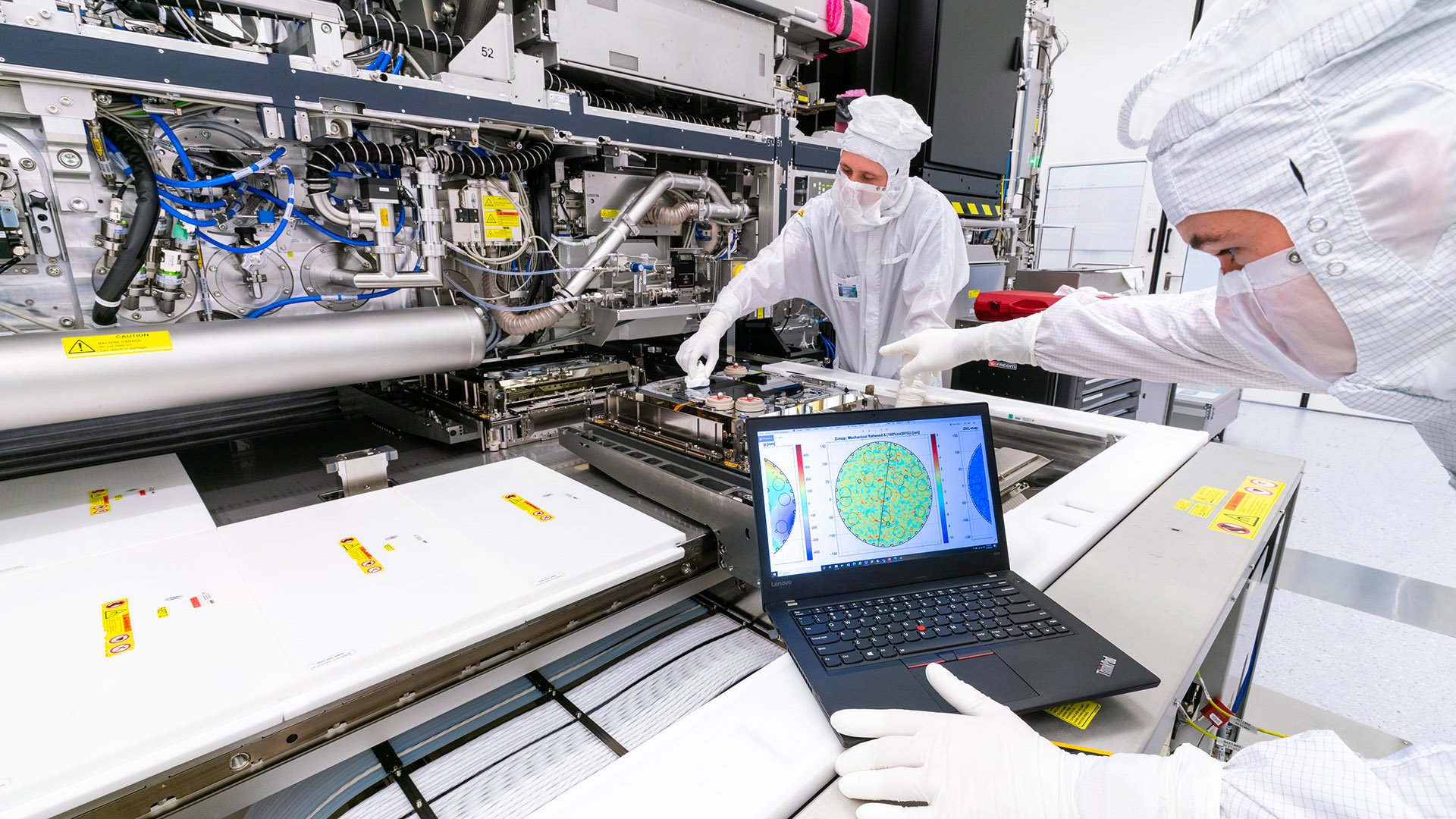 Two ASML engineers in white cleanroom suits use a laptop to test an EUV lithography machine in our factory in Veldhoven, the Netherlands. Two ASML engineers in white cleanroom suits use a laptop to test an EUV lithography machine in our factory in Veldhoven, the Netherlands.