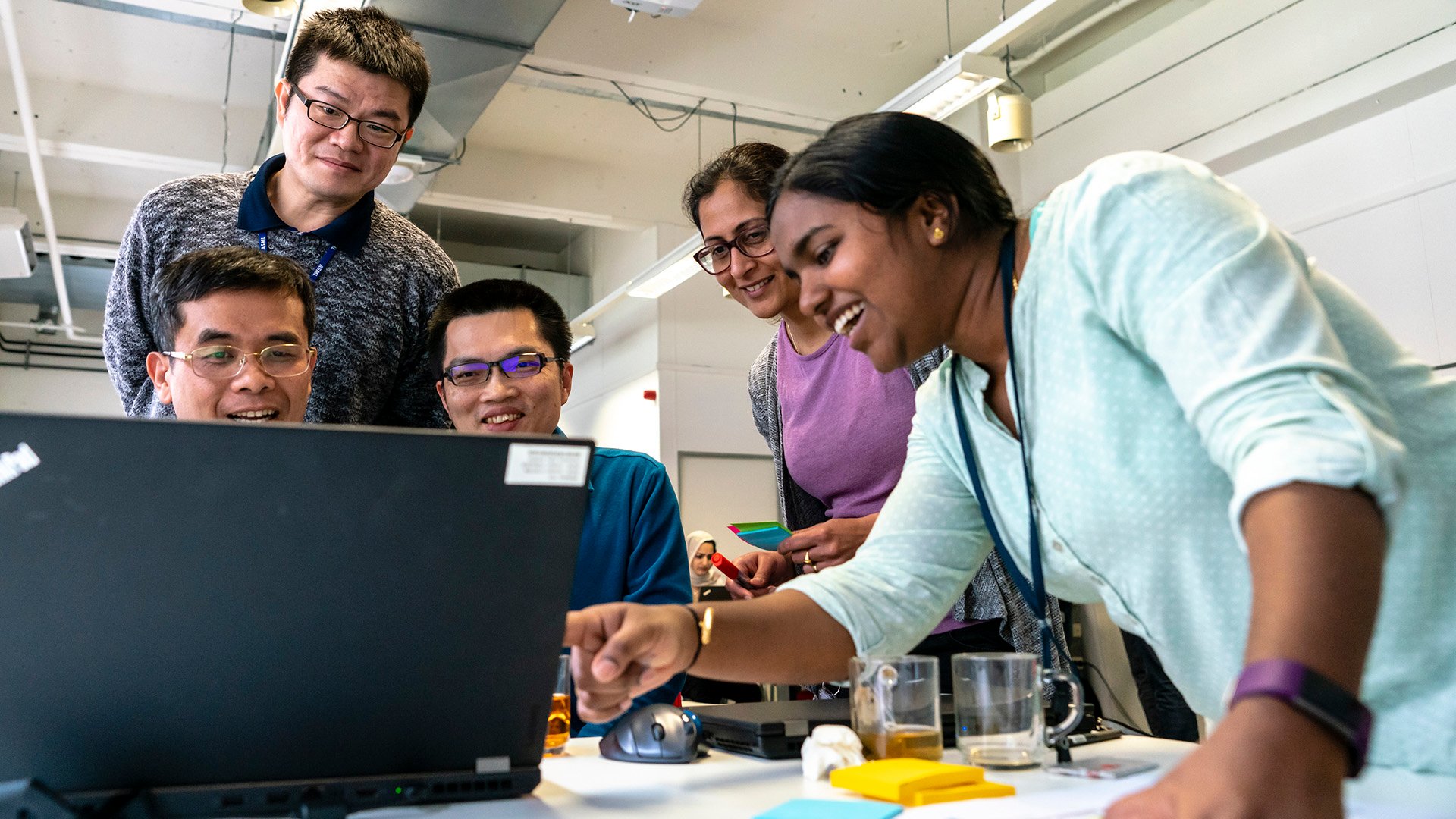 A young woman points to a laptop screen as other colleagues gather round a table at an ASML Agile event. A young woman points to a laptop screen as other colleagues gather round a table at an ASML Agile event.