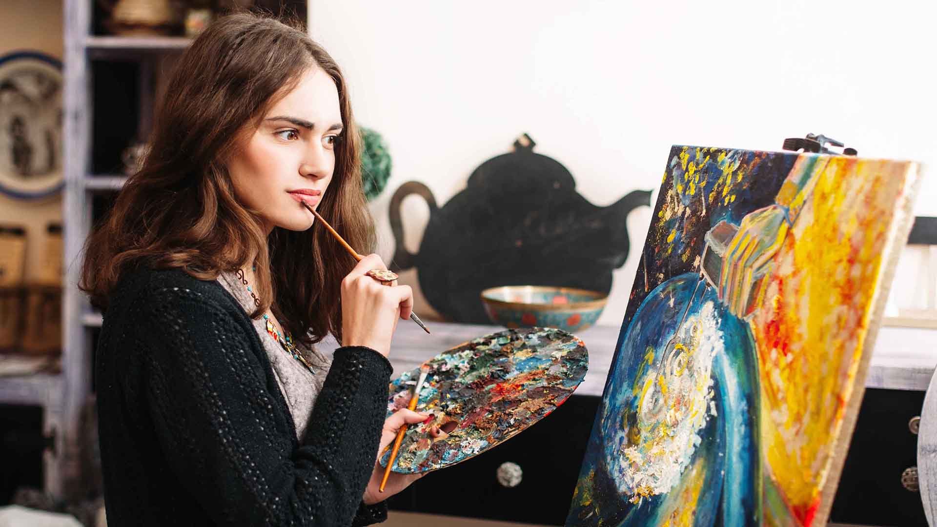 A woman holding a brush and palette in front of a painting. A woman holding a brush and palette in front of a painting.