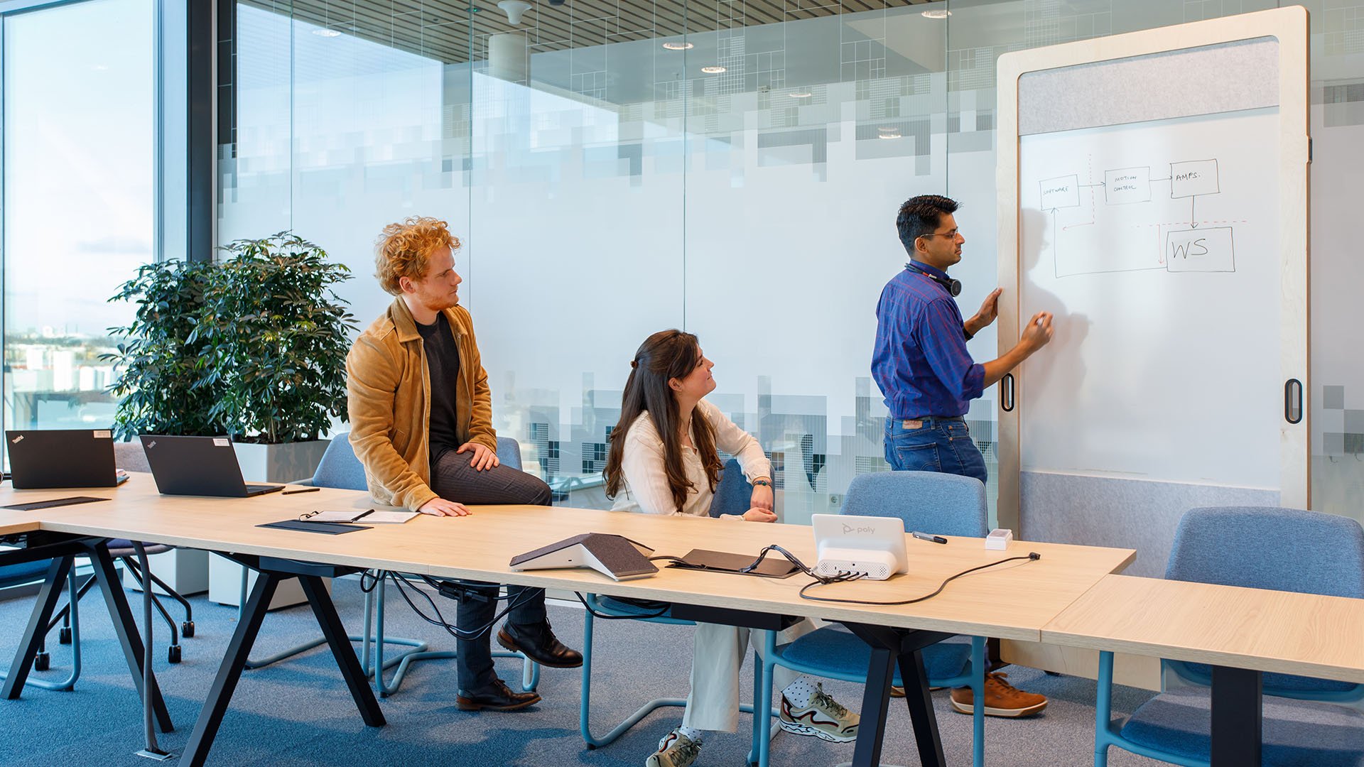 Two seated people watching another person write on a whiteboard Two seated people watching another person write on a whiteboard